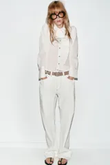 Camisa de manga larga con estampado de rayas verticales finas, cuello redondo con volante plisado y detalle de volante lateral en el frente. Cuenta con cierre frontal de botones y puños anchos.