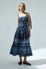 Vestido midi de algodón azul marino con estampado floral y geométrico en tonos celestes y blancos. Presenta escote recto, breteles ajustables con moñas, cuerpo entallado y falda acampanada con volados fruncidos en la parte inferior.