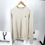 Buzo de punto color crema, de corte recto y manga larga. Tiene cuello redondo y logo bordado en el pecho.