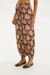 Pantalón babucha de tiro medio en tonos bordó y beige con estampado ornamental. Presenta cintura elastizada con cordón ajustable, diseño amplio y puños elastizados en los tobillos.