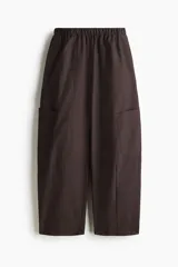 Pantalón cargo de corte holgado en color marrón, confeccionado en mezcla de algodón y nailon. Presenta cintura elástica de talle alto y perneras estilo globo con bolsillos tipo parche a los lados y costuras visibles en la parte delantera.