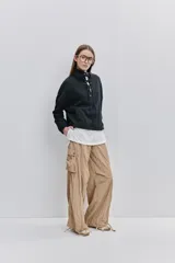 Pantalón cargo negro de corte relajado y pierna ancha con bolsillos laterales con solapa, cintura con doble broche y cierres metálicos en los tobillos.