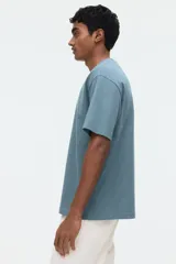 Remera de manga corta color verde, confeccionada en punto liviano, con cuello redondo ribeteado, hombros caídos, bajo recto y corte relajado.