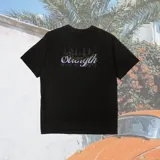 Remera negra de corte oversized con estampado en el centro de la espalda con la palabra "Strength" en tipografía cursiva con efecto de luces.