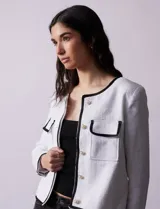 Chaqueta de tweed negra marca Nanette, con escote a la base, abertura central con botones, bolsillos delanteros, aplique de botones perlados en los puños, ribete en contraste blanco y forro interno.