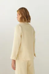 Chaqueta marrón de lana con cuello, solapa y bolsillos ojal. Forro solo en las mangas y terminaciones envivadas. Esquinas redondeadas y mangas con corte en puño que permiten transformarla en manga 3/4. Más larga en la espalda que en la delantera. Abrochadura con dos botones.