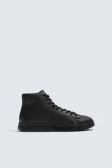 Zapatilla tipo botín de estilo minimalista fabricada en piel lisa de color negro. Presenta un diseño de caña media con cierre de cordones al tono y suela plana de goma a juego.