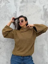Polera de tejido de punto acanalado en color ocre, con cuello alto y diseño de mangas amplias. Presenta un corte recto y holgado con un detalle de cuello abierto lateral.