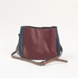 Cartera de hombro con diseño tricolor en tonos bordó, azul marino y tostado, confeccionada en cuero sintético con textura granulada. Incluye correa larga ajustable y cierre superior.