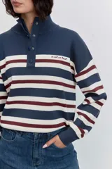 Sweater de punto con diseño a rayas horizontales en azul marino, blanco y bordó. Presenta cuello alto con cierre de botones a presión, mangas largas con puños acanalados y un pequeño bordado en el pecho.