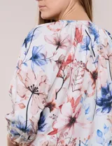 Blusa de gasa liviana blanca con estampado floral en tonos azules y rosados, escote en V, mangas 3/4 abullonadas con puños elásticos y corte fluido.
