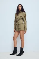 Chaqueta de estilo militar en color beige, con cuello subido, cierre frontal de botones, bolsillos de plastrón con solapa en el frente y detalle de hombreras con trabillas.