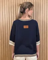 Buzo de punto color tostado, con mangas cortas holgadas y detalles de franjas en negro, blanco y beige en el cuello, los puños y el ruedo.