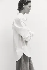 Camisa blanca de corte relajado, cuello clásico, mangas largas y cierre frontal con botones.