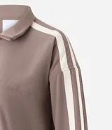 Campera deportiva oversized de microfibra color marrón, con cuello alto, cierre frontal y bolsillos laterales. Presenta bandas laterales contrastantes en las mangas y cordón ajustable en el dobladillo.