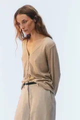Cardigan de punto fino color beige, con escote en V, cierre frontal de botones y mangas largas.