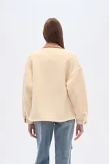 Campera tipo shacket de corderito color crema, con detalles en pana marrón en cuello, solapa de botones y bolsillos frontales. Diseño holgado de manga larga con cierre frontal de botones.
