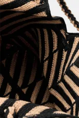 Bolso tipo shopper de yute 100%, con diseño de rayas y chevron en tonos negro y tostado, asas de hombro trenzadas y forma trapezoidal.