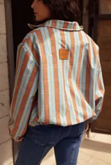 Campera impermeable con cierre frontal, diseño de rayas verticales en tonos celestes y marrones, cuello alto y puños elásticos.