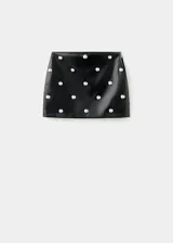 Minifalda de corte recto efecto piel, color negro, con diseño corto y adorno de tachuelas metálicas repartidas por la superficie. Cuenta con cierre de cremallera lateral y forro interior.