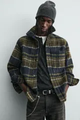 Sobrecamisa de corte relajado confeccionada en tejido con textura efecto pelo. Presenta diseño de cuadros en tonos verde y negro, cuello solapa, cierre frontal con botones, manga larga con puños abotonados y un bolsillo de plastrón en el pecho.