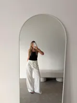 Pantalón de corte sastrero y pierna ancha, color beige con diseño de rayas verticales finas. Presenta pinzas en la cintura, cierre frontal con botón y bolsillos laterales.