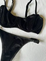 Conjunto de lencería de terciopelo negro, compuesto por un corpiño con aros y breteles regulables, y una bombacha con elásticos laterales ajustables.