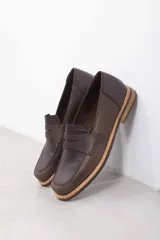 Mocasín de cuero vacuno en color marrón, con diseño bitono que combina texturas lisas y con grabado tipo cocodrilo en el empeine. Cuenta con detalle de estribo clásico y suela plana con vira en contraste.