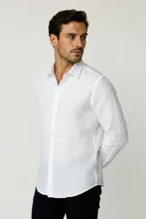 Camisa blanca de algodón, de diseño holgado y manga larga, con cuello camisero y cierre frontal de botones.