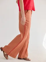 Pantalón de lino color ladrillo, de corte palazzo y tiro alto, con bolsillos laterales y vivos rojos a contratono.