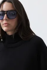 Polera de tejido liviano en color negro, con cuello alto, mangas largas y corte relajado. Presenta un diseño minimalista con recortes laterales que aportan estructura a la prenda.