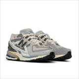 Championes New Balance modelo 1906, de estilo running urbano, con diseño técnico en tonos gris, plata y detalles en azul marino. Presenta una estructura de malla transpirable con refuerzos sintéticos, logo N lateral y entresuela con tecnología de amortiguación.