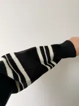 Buzo de punto negro con rayas horizontales blancas, de corte holgado y mangas largas.