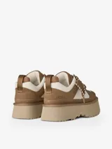 Sneakers UGG de plataforma con diseño chunky, confeccionadas en una combinación de gamuza marrón y paneles de nylon color crema. Presentan cordones gruesos trenzados, lengüeta acolchada y suela de plataforma dentada en tono beige.