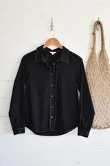 Camisa negra de manga larga con cuello clásico, cierre frontal con botones y volados verticales en el frente.