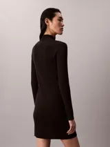 Vestido mini de punto acanalado color negro, de manga larga y cuello alto. Cuenta con una etiqueta con el logo de Calvin Klein en el centro del pecho.