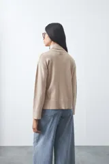 Polera de tejido liviano color negro con cuello alto y silueta relajada. Presenta mangas largas con puños ajustados y recortes laterales que aportan estructura al diseño.