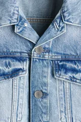 Campera trucker de denim de algodón rígido en color celeste con lavado claro, cuello camisero, cierre frontal de botones metálicos, bolsillos con solapa en el pecho y bolsillos laterales.