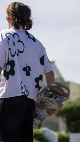 Camisa de manga corta, color blanco, con estampado de flores grandes en verde oscuro. Tiene cuello camisero y cierre frontal de botones.
