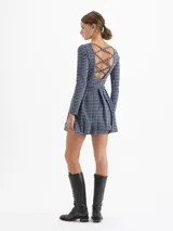 Vestido corto de punto con estampado de cuadros tipo príncipe de gales en tonos azul, negro y blanco. Presenta escote redondo, mangas largas y falda con diseño balloon que aporta volumen. Cuenta con espalda abierta con tiras cruzadas.