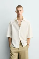 Camisa de corte relajado y boxy fit, confeccionada en tejido con textura irregular. Presenta cuello solapa, manga corta y cierre frontal con botones.
