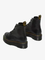 Bota Dr. Martens modelo Sinclair, color negro, de cuero Milled Nappa con textura granulada. Presenta una cremallera frontal extraíble, cordones, y se asienta sobre una suela de plataforma gruesa con costuras amarillas distintivas y una trabilla amarilla en el talón.