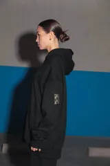 Buzo negro oversize de frisa con capucha amplia, bolsillo canguro, terminaciones de puño y ruedo con rib, y logo bordado en el centro delantero.
