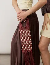 Cartera tipo bolso de mano confeccionada mediante técnica de tejido de red en cordón marrón, decorada con cuentas de madera y detalles de flecos en la parte inferior.