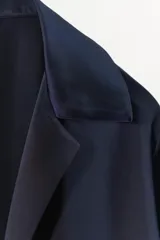 Camisa de manga larga color azul marino, confeccionada en tejido satinado. Presenta cuello solapa, puños anchos y cierre frontal mediante lazada ajustable en el centro.