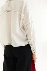 Camisa de corte oversize y estilo casual, confeccionada en algodón negro con costuras a contratono en color blanco. Presenta cuello camisero, cierre frontal parcial, mangas largas y un bordado distintivo en el puño.