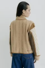 Chaqueta de punto con diseño color block en negro, beige y marrón. Presenta cuello redondo, cierre frontal con botones grandes, bolsillos frontales y detalles de costuras decorativas verticales en color claro.