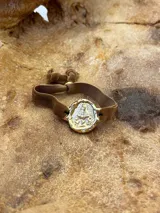 Pulsera dorada con dije redondo con la imagen de la Virgen de Fátima y cinta de terciopelo elástico color verde petróleo.