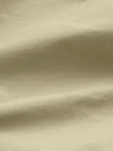 Camisa oversized color beige, confeccionada en algodón regenerativo, con cuello en punta, puños segados, bajo redondeado, plisado trasero central, bolsillo de parche en el pecho y cierre de botones.