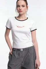 Remera baby blanca de algodón, de corte cropped al cuerpo y mangas cortas. Presenta ribetes negros en contraste en el cuello redondo y los puños, con un estampado localizado de un ají rojo con la inscripción 'Pimentón' en el centro del pecho.